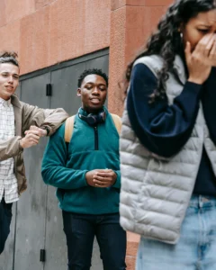 Jeune fille bouleversée qui s’éloigne pendant que deux adolescents derrière elle l’intimident et envahissent son espace.